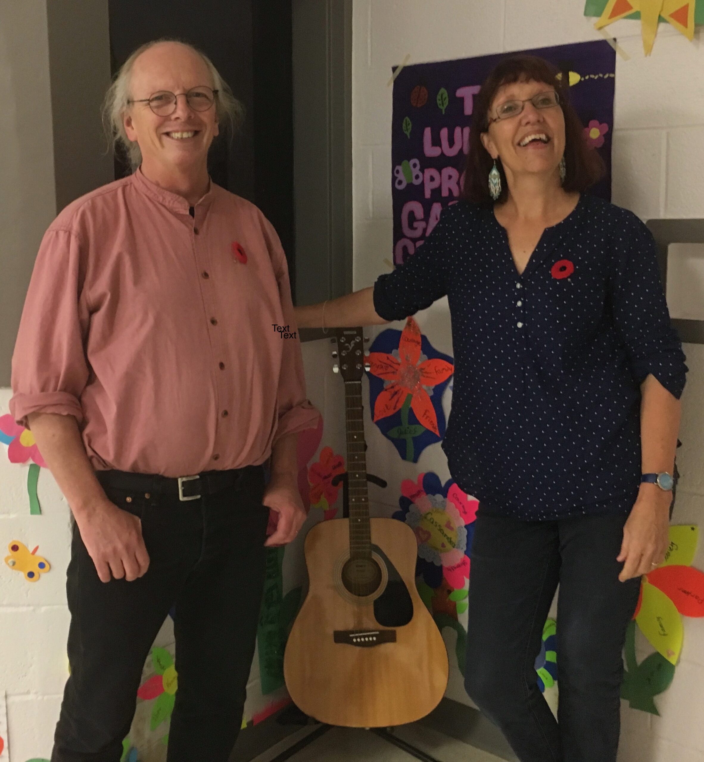 A smiling man and woman standing either side of a guitar.